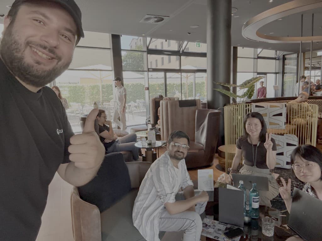 Group selfie at a Café Cursor meetup with builders working on laptops